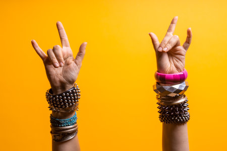 Hand gestures. Thumbs up, thats a cool gesture of the rocker. womens hand with lots of bracelets, youth fun style. bright yellow backgroundの写真素材