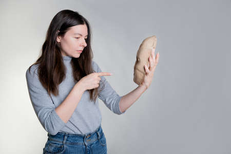 Self-criticism, a young woman criticizes a part of herself, a concept. holds a mask in her hands and scolds her. Photo on grayの写真素材