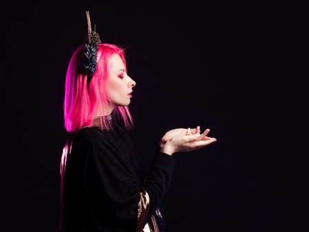 A Gothic queen in a crown with roses and rays. Young woman with pink hair in a mystical image, portrait on blackの写真素材