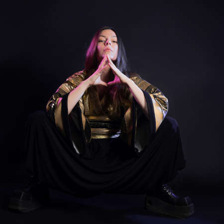 Stylish and daring image, futuristic fashion. A young woman in a multicultural outfit mixing Asian and European style, a golden kimono shirt and trousers, photo in the studio on blackの写真素材