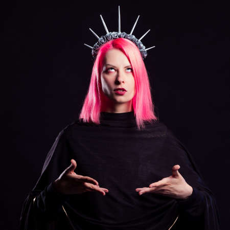 A gothic diva with pink hair in a royal image, a crown with roses and rays on her head, open arms stretched out to youの写真素材
