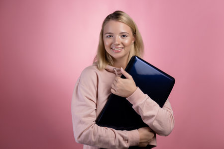 A young blonde woman with a square haircut, holds a closed laptop in hands and adjusts glasses. Student or freelancerの写真素材
