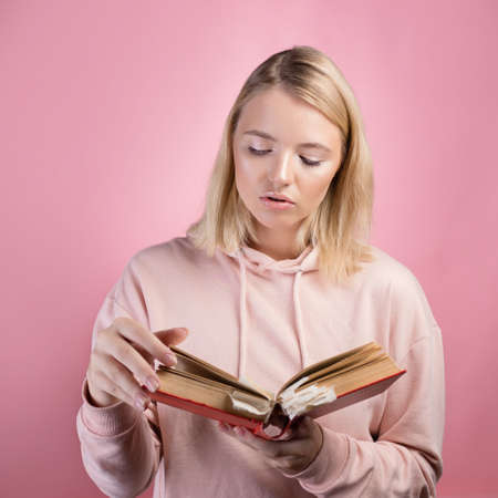 Fascinating reading, serious study of educational materials, an open book with a large number of bookmarks in the hands of a student. A young woman in a pink hoodie with a textbook in her hands,の写真素材