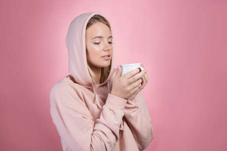 Drink a hot drink, keep warm in cold weather. A young woman with a hood on her head drinks a hot seasonal drink, tea, coffee or mulled wineの写真素材