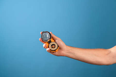 Help in navigating the terrain, find your location, concept. Magnetic compass in a mans hand, photo on a blue backgroundの写真素材