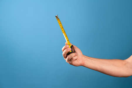 Measure it, a yellow construction tape measure to measure the length of something. Roulette with a measured segment in a mans hand, blue backgroundの写真素材