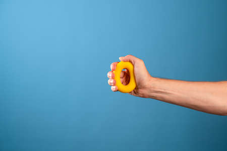 Squeeze, apply force. Soft toroidal rubber expander for the development of palm muscles in the male hand, blue backgroundの写真素材