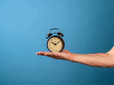 Hurry up, its time to act, concept. A mans hand holds a vintage alarm clock, a photo on a blue backgroundの写真素材