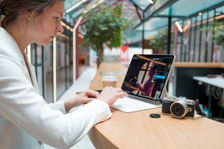 A photographer or retoucher works remotely with a laptop in a public space or coworking. A young brunette in a white jacket works with images, a designer or a social media managerの写真素材