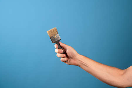 Update the interior, paint the walls, decor in the house. A mans hand stretches out a paint brush, blue backgroundの写真素材