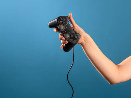 Play computer games ,become a professional gamer. A female hand holds a gamepad with a wire, a photo on a blue backgroundの写真素材