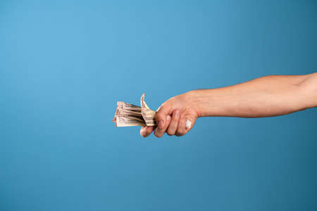 Earn money, get a good revenue. A mans hand and a lot of cash, a photo on a blue backgroundの写真素材
