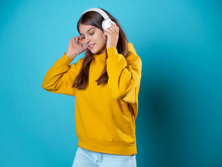 A music lover, A charming young woman with headphones, listens to music. A young brunette in a bright yellow hoodie uses a mobile app to listen to audioの写真素材
