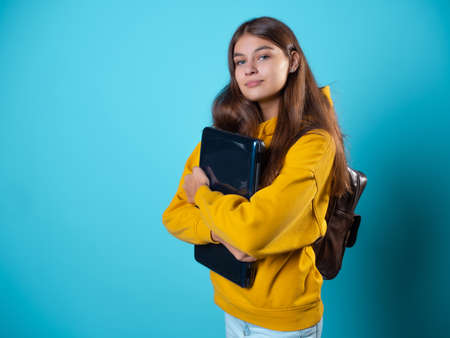 Internet work and e-education, a student or a freelancer works remotely. A student with a laptop in her hands, a young brunette in a yellow hoodie on a blue backgroundの写真素材
