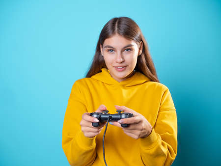 A young woman in a yellow hoodie clutches a gamepad in her hands and looks at the monitor, a gamer in the process of playing on the console , an exciting gameplayの写真素材