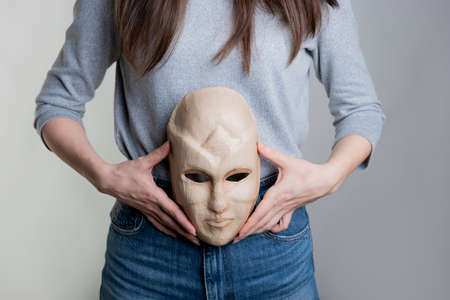 A young woman holds a mask with her face at the level of her stomach. The concept of the inner world, pregnancy or the microflora of the body.の写真素材