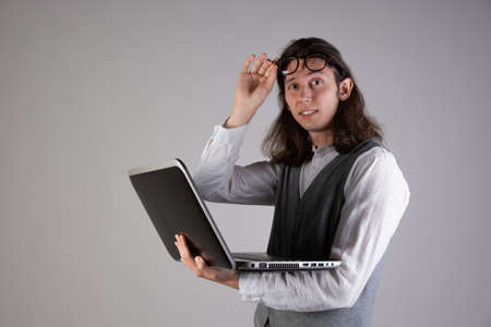 Training and new technologies, online courses, e-learning. A young man with long hair and glasses. A student is holding a laptopの写真素材