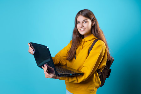 Work and study remotely, a new normal, a concept. A student with a laptop in her hands, a young brunette in a yellow hoodie on a blue backgroundの写真素材