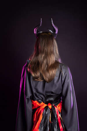 A demoness with horns and in a black kimono with a red belt, a costume of a mystical creature, a young woman in a fantasy gothic image, back viewの写真素材