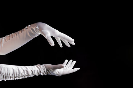 Hand gestures. Lady illusionist, beautiful hands in long white gloves make a spell. Shows and tricks and illusions, hands are drawn to the right side.の写真素材