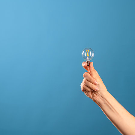 Take a small idea and create something big, new and innovative. A small vintage incandescent lamp in a female hand, blue background.の写真素材
