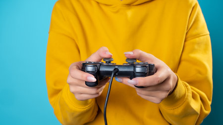 A young woman in a yellow hoodie clutches a gamepad in her hands, a frontal view of a close-up hand, a gamer in the process of passing the game, fascinating gameplayの写真素材