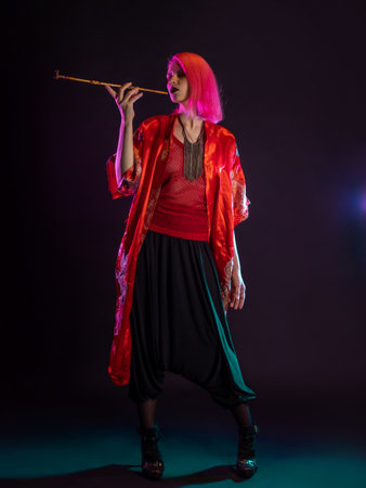 Futuristic look, multicultural outfit, young woman with pink hair in modern trousers, vintage kimono and smoking a pipe in her handsの写真素材