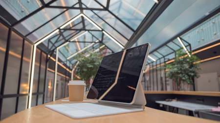 freelancers workplace. A thin mobile laptop on a table in a coworking or other public space. low depth of field. tablet computer with a code on the screen and coffee to take away.の写真素材