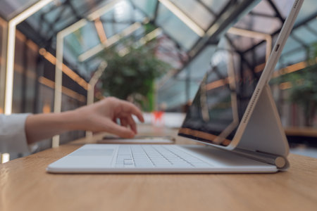 Remote work or freelance, modern opportunities for a mobile lifestyle. Womens hands are typing on keyboard of tablet computer, close-up side view, public space hall on background, low depth of field.の写真素材
