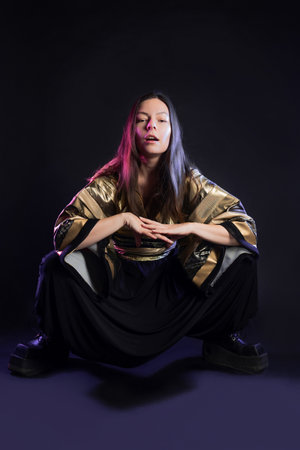 Stylish and daring image, futuristic fashion. A young woman in a multicultural outfit mixing Asian and European style, a golden kimono shirt and trousers, photo in the studio on blackの写真素材