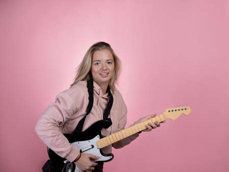 Play the guitar, pretend that you are a guitarist, a game guitar. Young woman on a pink backgroundの写真素材