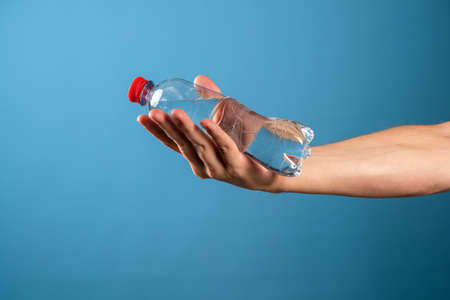 Drink water. The benefits of drinking clean water for the health of the body and well-being. A mans hand hands you a bottle of liquid. Blue background.の写真素材