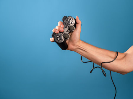 Play computer games ,become a professional gamer. A mans hand holds a gamepad with a wire, a photo on a blue backgroundの写真素材