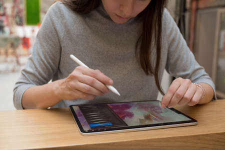 A digital artist draws on a graphic screen tablet using a stylus, a freelancer works in a public space coworking, the ability to work remotely. A young woman artist or designer uses a tablet to drawの写真素材