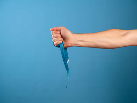 Lose weight, get rid of excess weight, a call to engage in health. A mans hand holds a centimeter ribbon in his fist, blue backgroundの写真素材