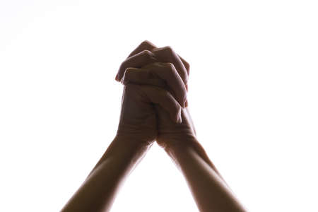 Praying crossed hands on a white background. Light from above. Hands folded in prayer. Hand gesturesの写真素材