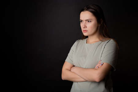 Suspicions, a look from the left. A young brunette woman in a T-shirt, experiencing distrust and doubt, portrait on blackの写真素材