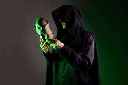 An anonymous villain, a hidden figure in a black cape with a hood. A mystical character with a mysterious mask in his handsの写真素材