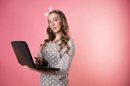 young woman cook or pastry chef runs a business and takes orders in an online store, a cook in an apron holding a laptop in her hands. pastry chef in an apron on a pink background.の写真素材