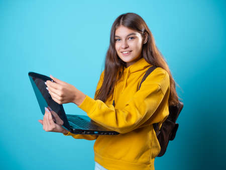 Work and study remotely, a new normal, a concept. A student with a laptop in her hands, a young brunette in a yellow hoodie on a blue backgroundの写真素材
