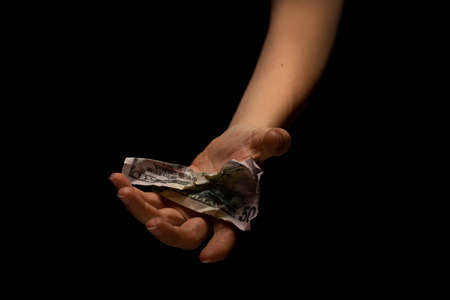 Giving Alms to the poor. Inflation and economic problems, unemployment and lack of money, concept. Hands with cash in a dark key on a black backgroundの写真素材