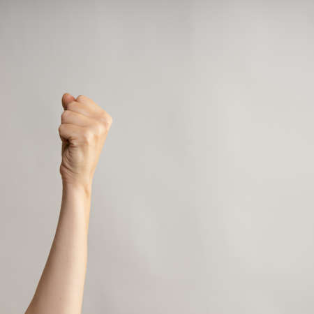 Hand gestures. womans fist stretches up, a symbol of the struggle for rights and dissent. Hand gestures, light grey backgroundの写真素材