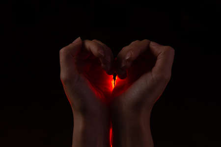 Two hands folded in the shape of a heart, light inside. Clench your hands, symbol of love. Black backgroundの写真素材