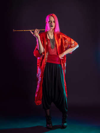 Futuristic look, multicultural outfit, young woman with pink hair in modern trousers, vintage kimono and smoking a pipe in her handsの写真素材