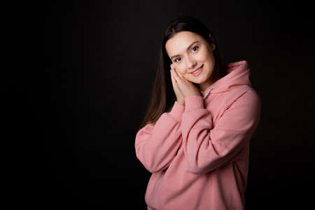 Cute young brunette in a pink hoodie, portrait on a black background.の写真素材