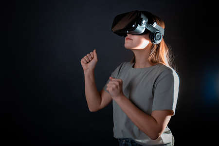 Virtual experience, a young woman using virtual reality glasses, playing a game or interacting with a metaverse, portrait on a black backgroundの写真素材