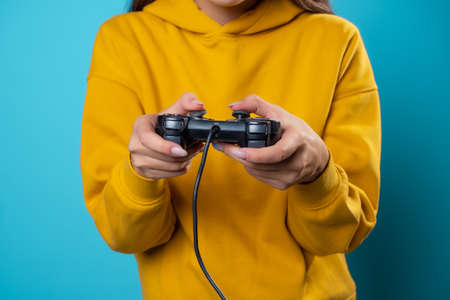A young woman in a yellow hoodie clutches a gamepad in her hands, a frontal view of a close-up hand, a gamer in the process of passing the game, fascinating gameplayの写真素材