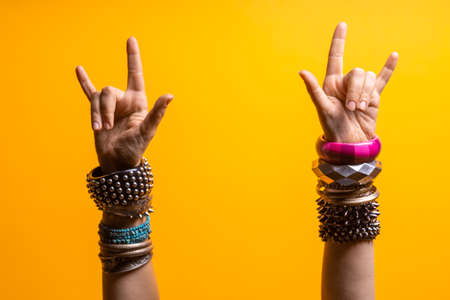 Hand gestures. Thumbs up, thats a cool gesture of the rocker. womens hand with lots of bracelets, youth fun style. bright yellow backgroundの写真素材