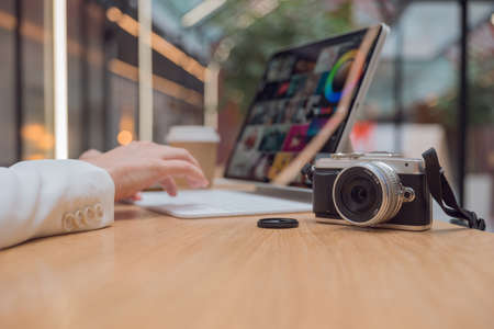 A photographer or retoucher works remotely with a laptop in a public space or coworking. A young woman in a white jacket works with images, a designer or a social media managerの写真素材