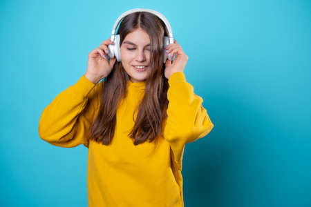 A young smiling student wearing headphones, listening to music. A young brunette in a bright yellow hoodie uses a mobile app to listen to audioの写真素材